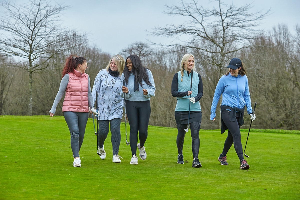 A group of women golfers on the golf course enjoying spending time together walking and holding their women's gold clubs.